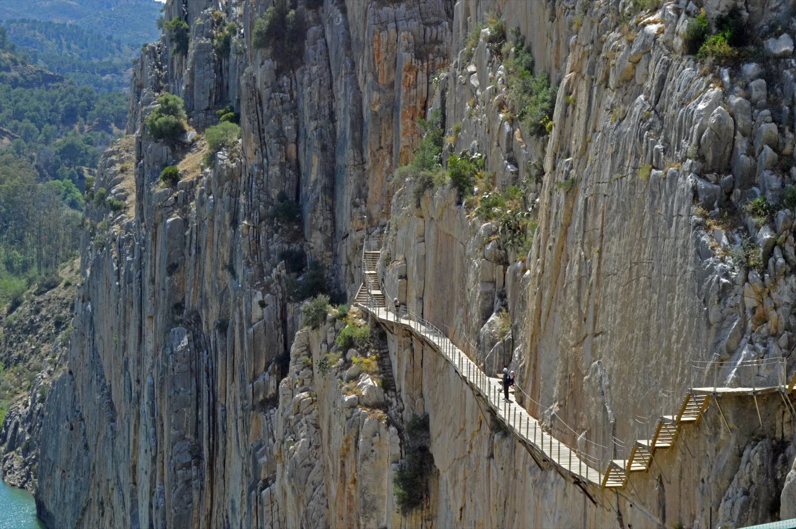 The modern wooden Caminito del Rey boardwalk zig-zagging with staircases as it clings to a sheer grey limestone cliff face high in the Gaitanes Gorge
