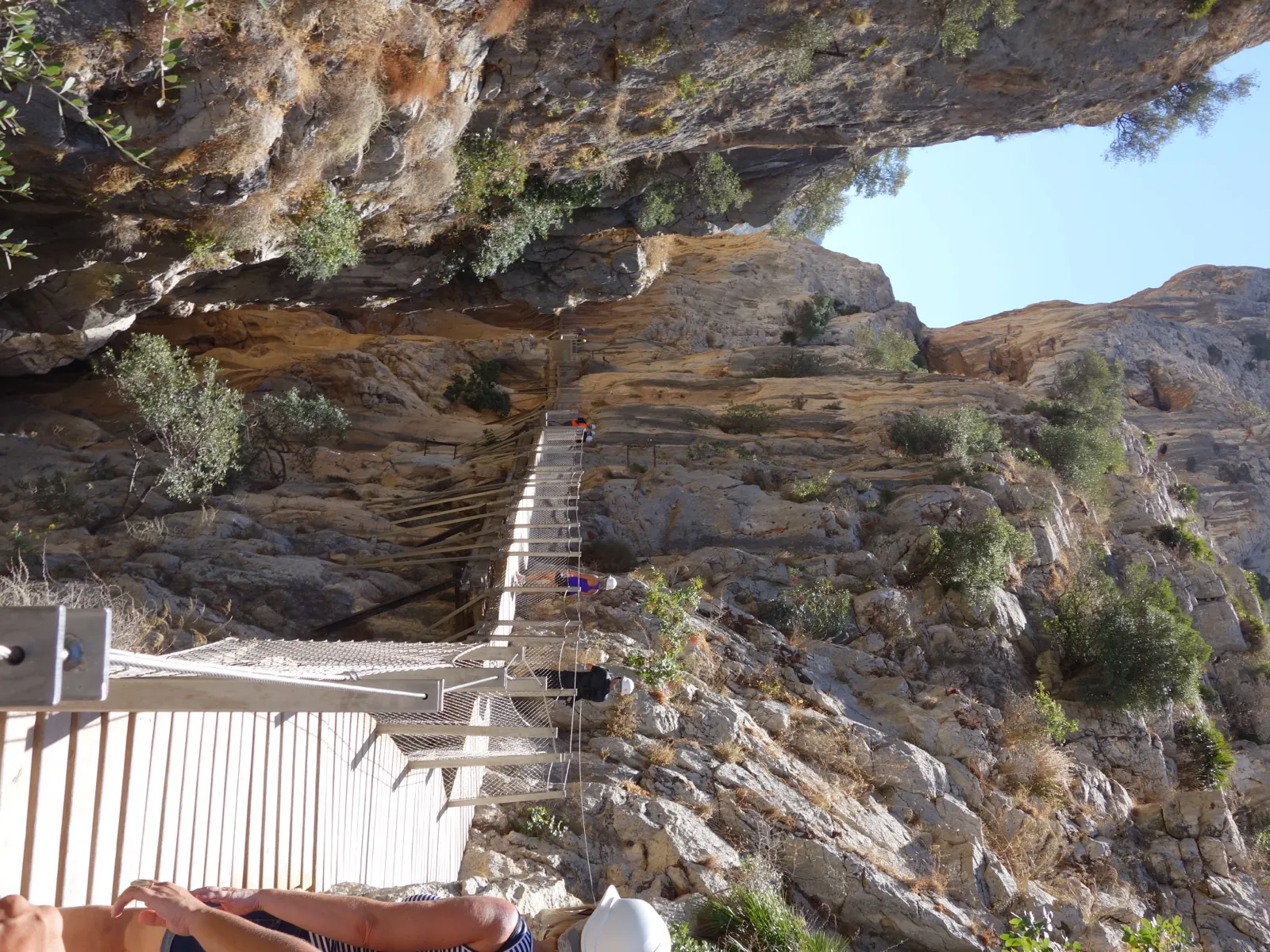 Visitors in safety helmets on the Caminito del Rey boardwalk passing beneath a huge overhanging limestone arch near the northern Gaitanejo entrance